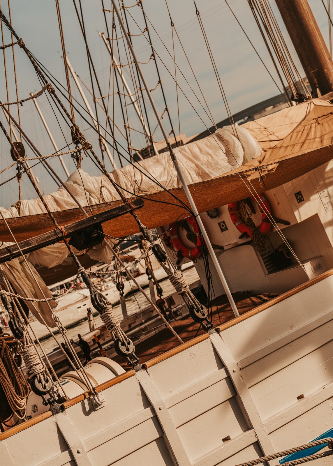 Rigging, a furled sail and life rings on the deck of a wooden sailing ship, seen at a tilt